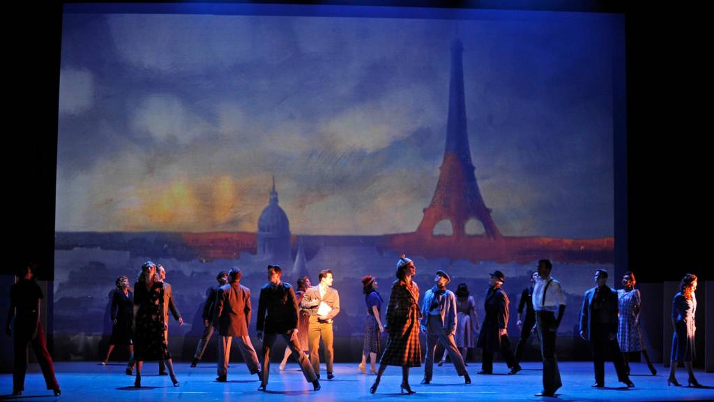 Groupe d'acteurs devant une peinture géante d'un lever de soleil sur Paris avec la tour Eiffel