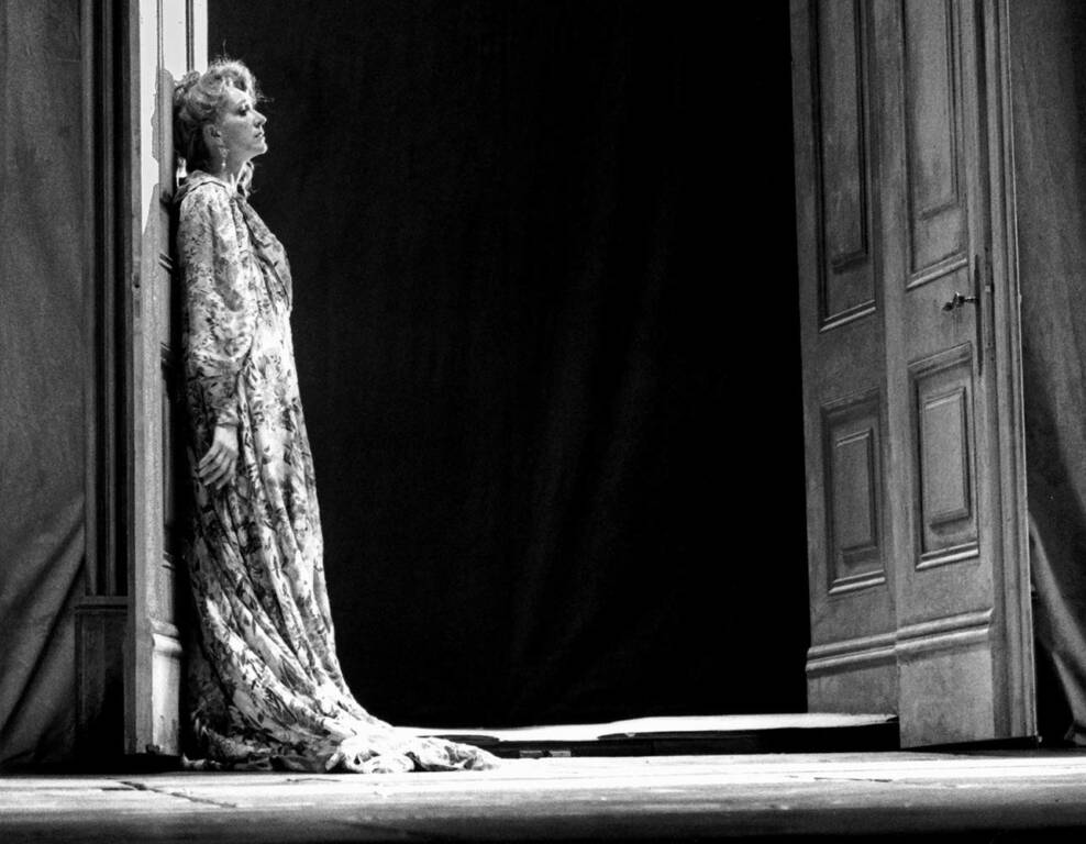 Une femme en robe longue s'appuie sur le montant d'une porte