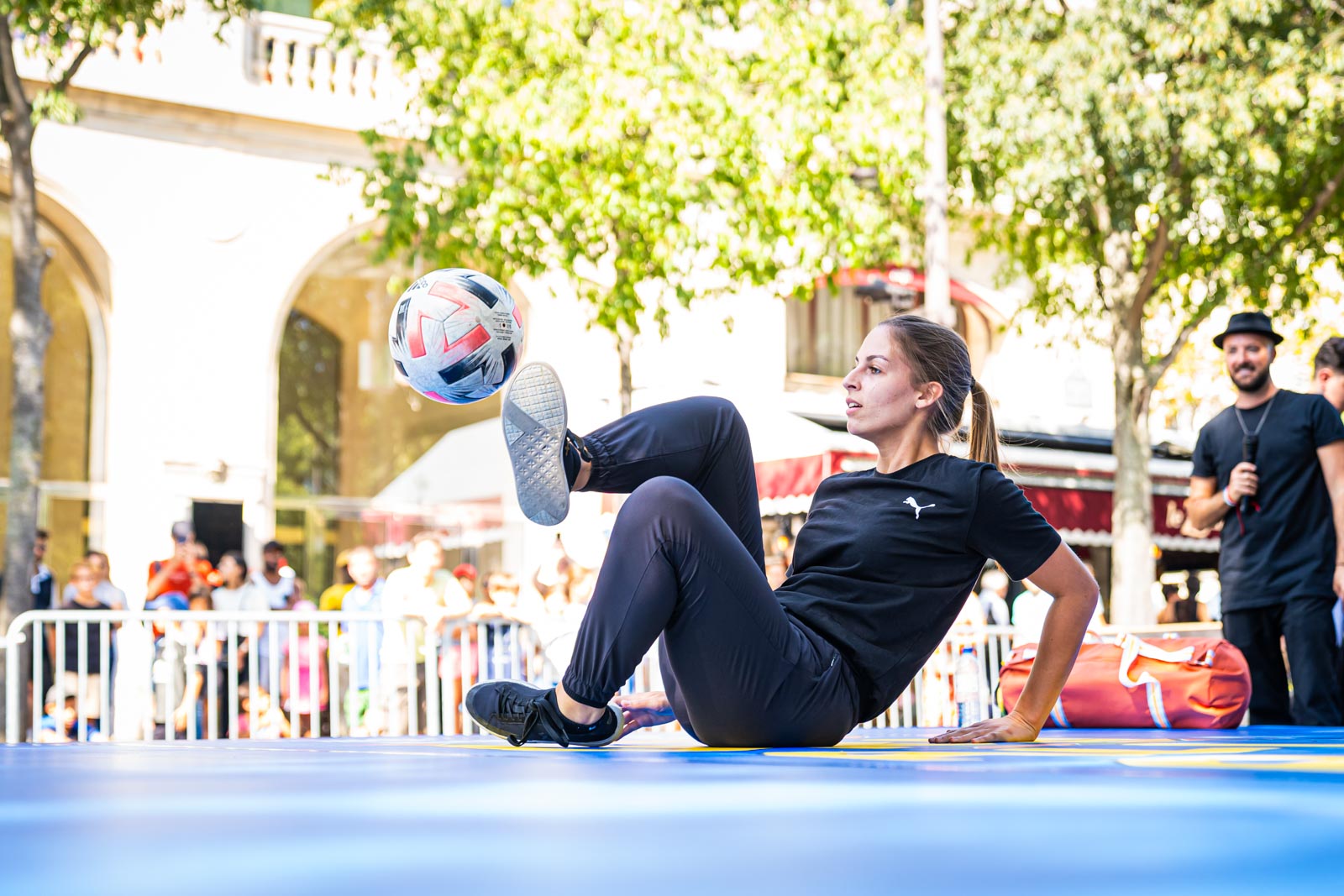 Une jeune femme assiste sur une estrade fait sauter une balle de foot avec ses jambes