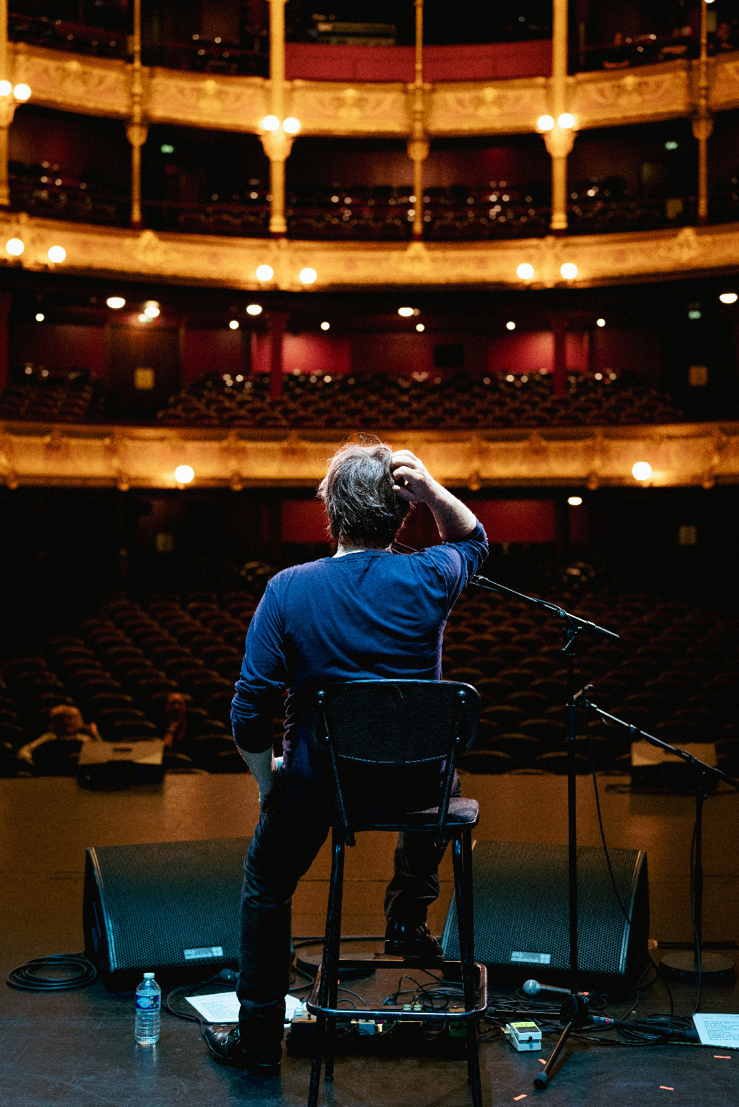 Un homme de dos se gratte la tête devant une grande salle vide