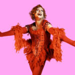 Un homme travesti en danseuse de cabaret en corset rouge avec plumes et hauts talons